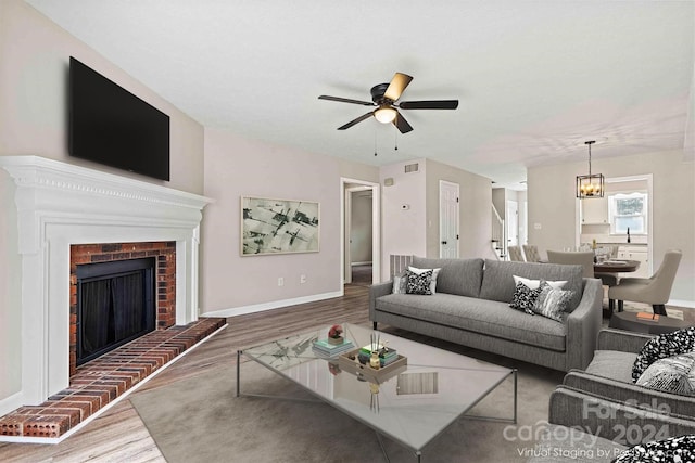 living room featuring a fireplace, wood-type flooring, and ceiling fan with notable chandelier