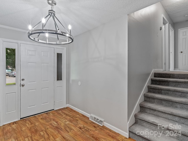 foyer entrance with wood-type flooring, a textured ceiling, and a notable chandelier