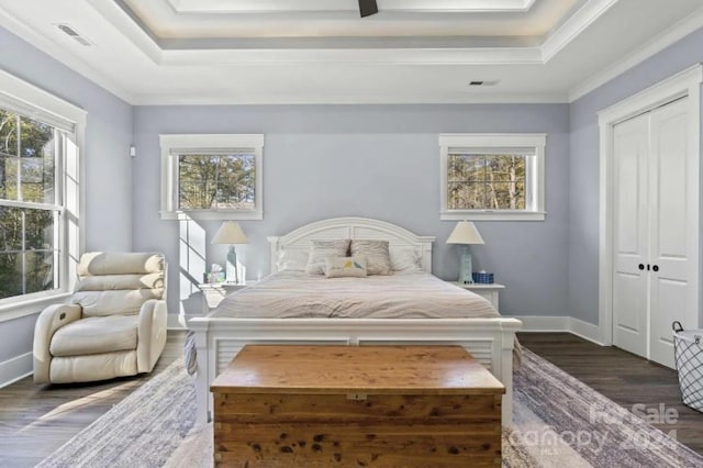 bedroom with dark hardwood / wood-style flooring, a tray ceiling, a closet, and crown molding