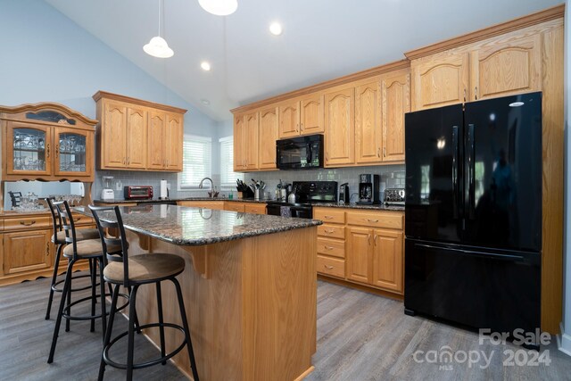 kitchen with wood-type flooring, black appliances, tasteful backsplash, and a center island