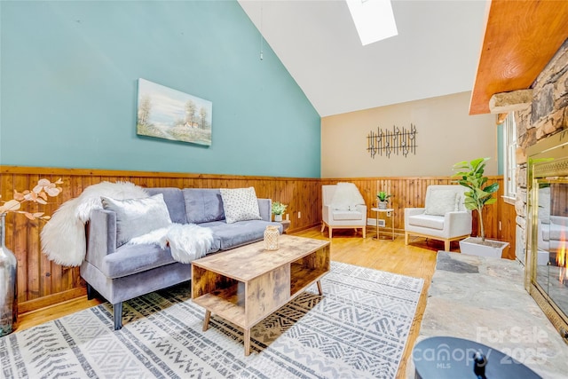 living room with light hardwood / wood-style floors, vaulted ceiling with skylight, and a stone fireplace