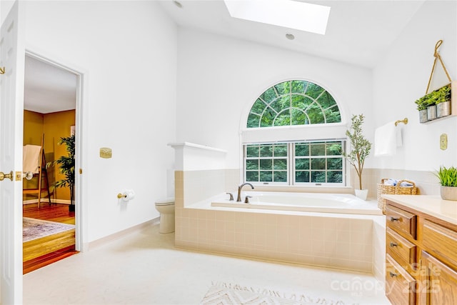 bathroom featuring toilet, tiled tub, a skylight, and vanity