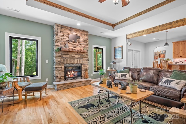 living room featuring ornamental molding, a raised ceiling, ceiling fan, a fireplace, and light hardwood / wood-style floors