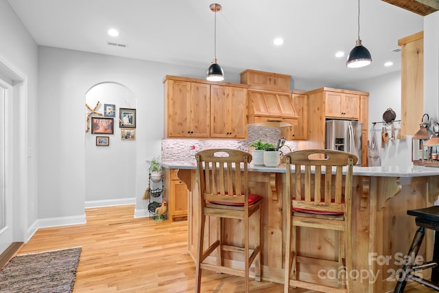 kitchen featuring decorative backsplash, custom range hood, pendant lighting, stainless steel fridge with ice dispenser, and light hardwood / wood-style floors