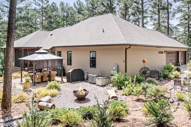 rear view of house with central AC, a gazebo, an outdoor living space with a fire pit, a garage, and a patio