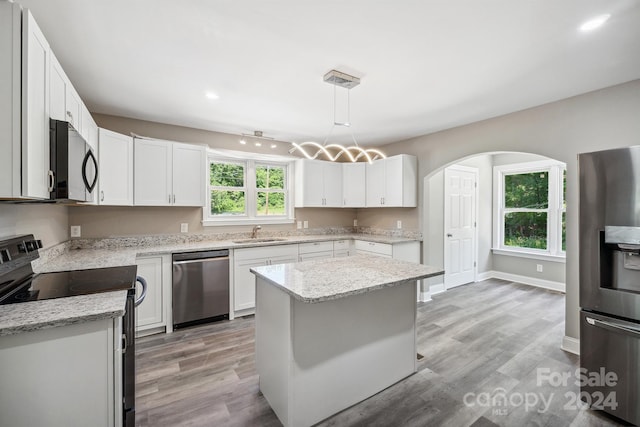 kitchen with appliances with stainless steel finishes, a kitchen island, sink, white cabinetry, and hanging light fixtures