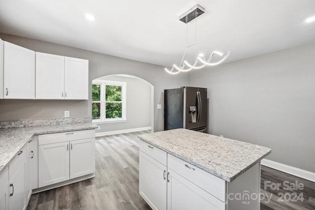 kitchen with light stone counters, white cabinetry, hanging light fixtures, and stainless steel refrigerator with ice dispenser