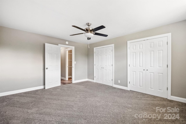 unfurnished bedroom featuring two closets, dark carpet, and ceiling fan