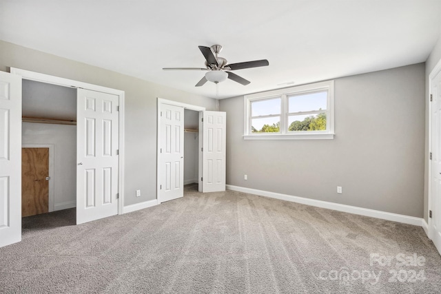 unfurnished bedroom featuring ceiling fan, carpet floors, and two closets