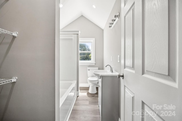 bathroom featuring a tub, hardwood / wood-style floors, lofted ceiling, toilet, and vanity