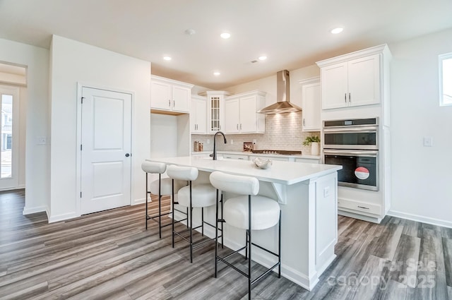 kitchen with appliances with stainless steel finishes, tasteful backsplash, white cabinetry, an island with sink, and wall chimney range hood