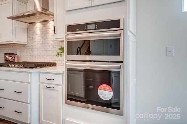 kitchen featuring white cabinetry, wall chimney exhaust hood, stainless steel appliances, and tasteful backsplash