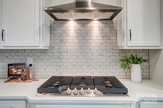 kitchen with stainless steel gas cooktop, wall chimney range hood, white cabinets, and decorative backsplash