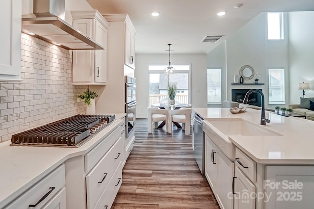 kitchen with pendant lighting, sink, stainless steel appliances, white cabinets, and wall chimney exhaust hood