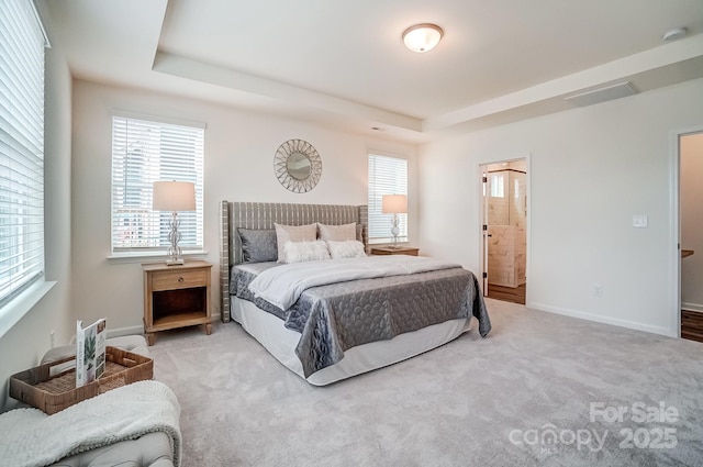 bedroom featuring ensuite bathroom, a tray ceiling, and light carpet