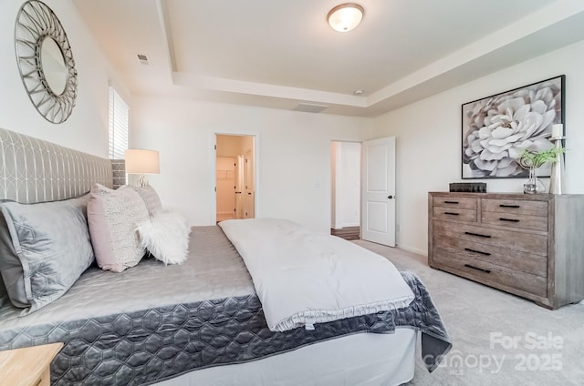 bedroom with light colored carpet, ensuite bath, and a tray ceiling