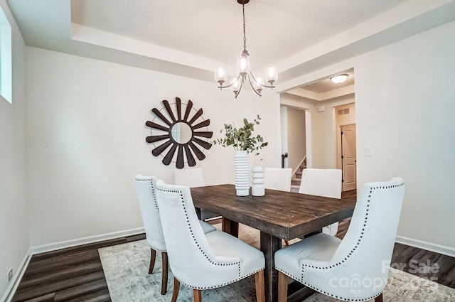 dining space featuring dark hardwood / wood-style floors, an inviting chandelier, and a tray ceiling