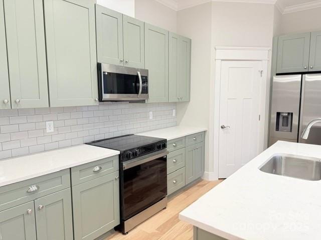 kitchen with sink, light wood-type flooring, stainless steel appliances, ornamental molding, and tasteful backsplash