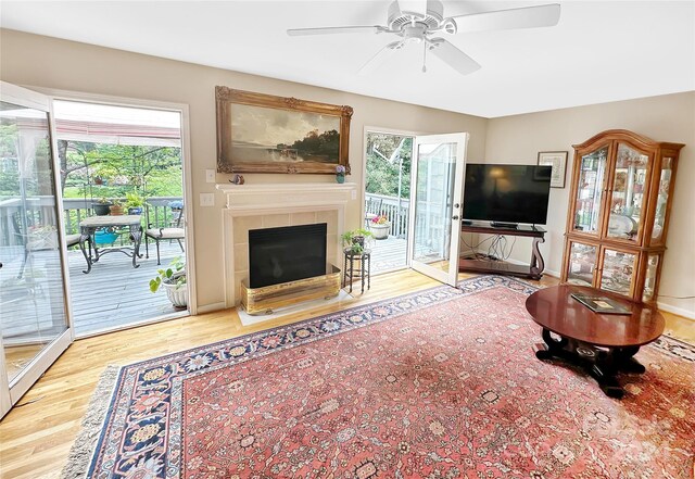 living room with a tiled fireplace, light hardwood / wood-style flooring, and ceiling fan