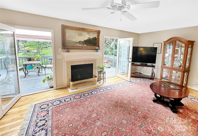 living room featuring light hardwood / wood-style floors, ceiling fan, a tiled fireplace, and a healthy amount of sunlight