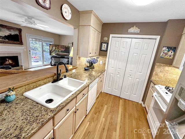 kitchen with decorative backsplash, white appliances, light wood-type flooring, a tile fireplace, and sink