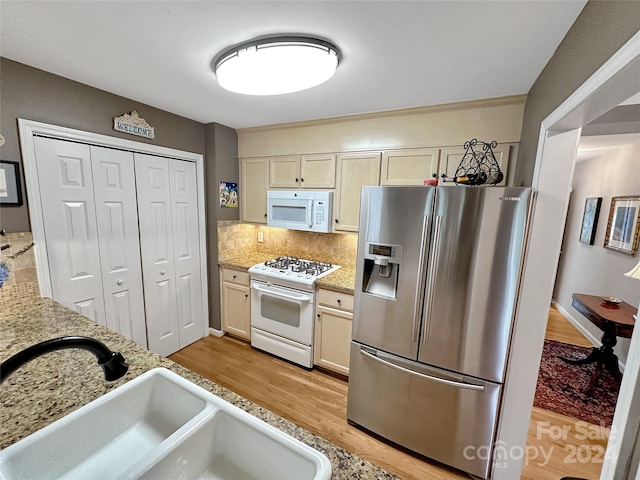 kitchen featuring light stone countertops, white appliances, decorative backsplash, sink, and light hardwood / wood-style flooring