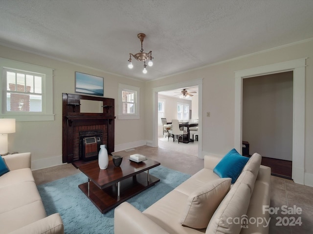 living room with ornamental molding, a brick fireplace, a chandelier, and a textured ceiling