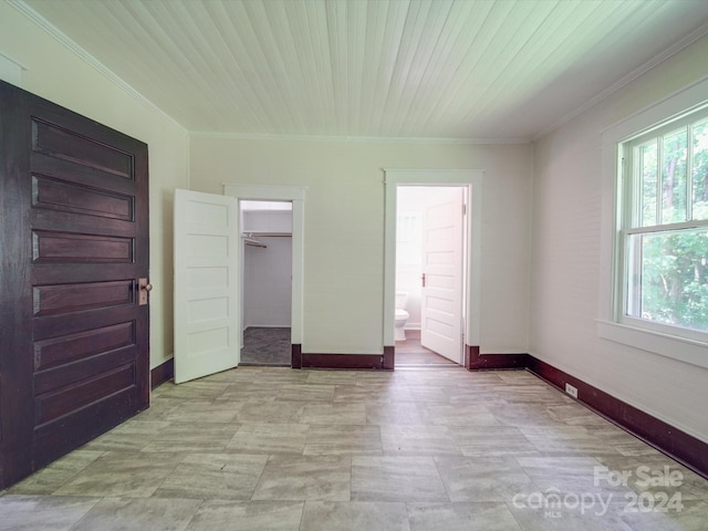 unfurnished bedroom with crown molding, a walk in closet, connected bathroom, and a closet