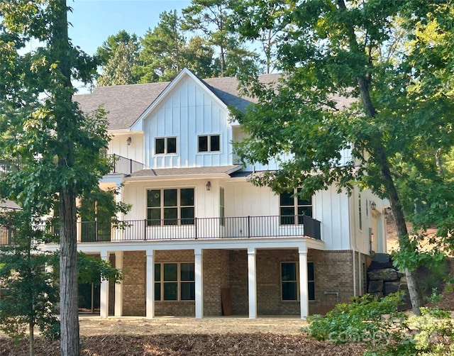 back of house with board and batten siding, brick siding, a balcony, and roof with shingles