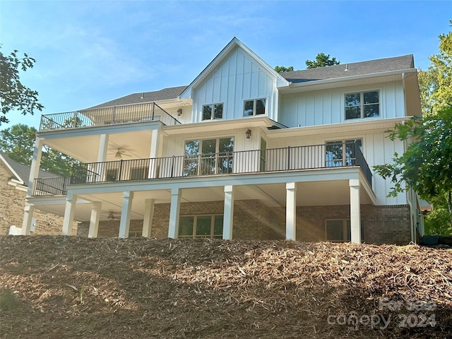 rear view of house with brick siding, a shingled roof, board and batten siding, a ceiling fan, and a balcony