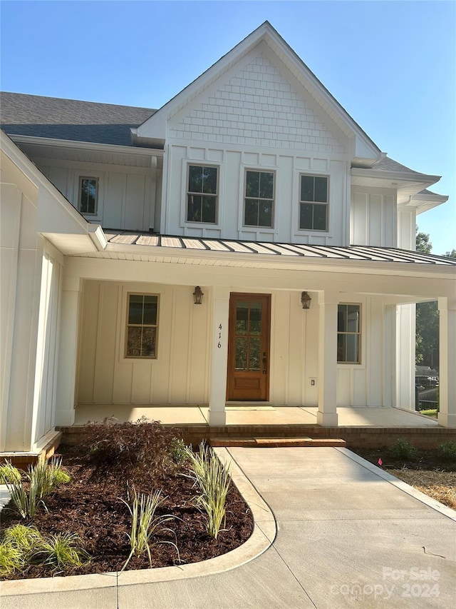 doorway to property with a shingled roof, covered porch, board and batten siding, a standing seam roof, and metal roof