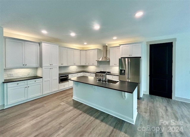 kitchen with a sink, light wood-style floors, wall chimney range hood, appliances with stainless steel finishes, and dark countertops