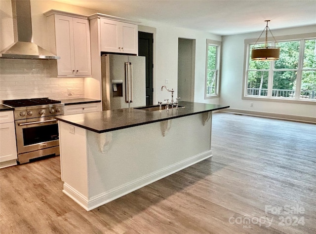 kitchen featuring dark countertops, light wood-style flooring, appliances with stainless steel finishes, wall chimney range hood, and a sink