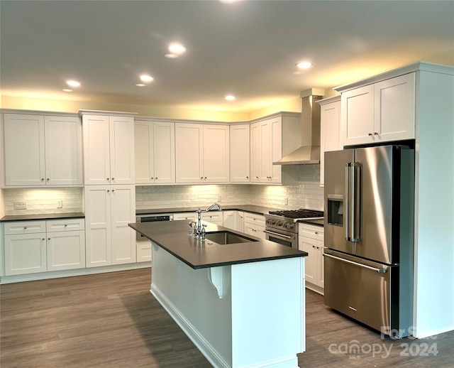 kitchen featuring stainless steel appliances, dark countertops, dark wood-type flooring, a sink, and wall chimney range hood