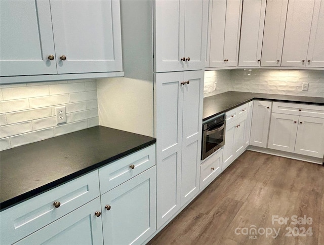 kitchen featuring dark wood finished floors, decorative backsplash, white cabinets, dark countertops, and stainless steel oven