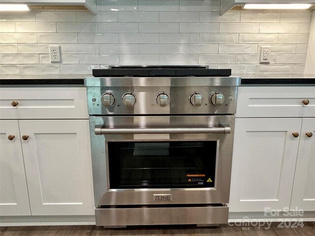 kitchen featuring tasteful backsplash, high end stainless steel range, dark countertops, and white cabinetry