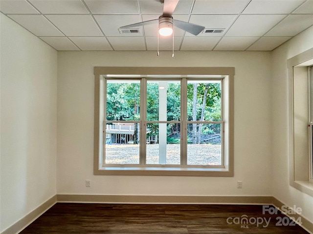 empty room with a paneled ceiling, dark wood finished floors, a wealth of natural light, and a ceiling fan