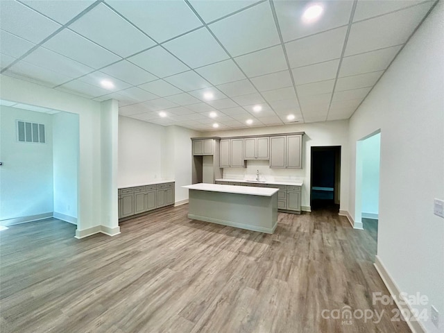 kitchen with light wood finished floors, visible vents, a kitchen island, gray cabinets, and light countertops