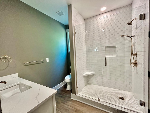 bathroom featuring visible vents, toilet, a stall shower, wood finished floors, and baseboards