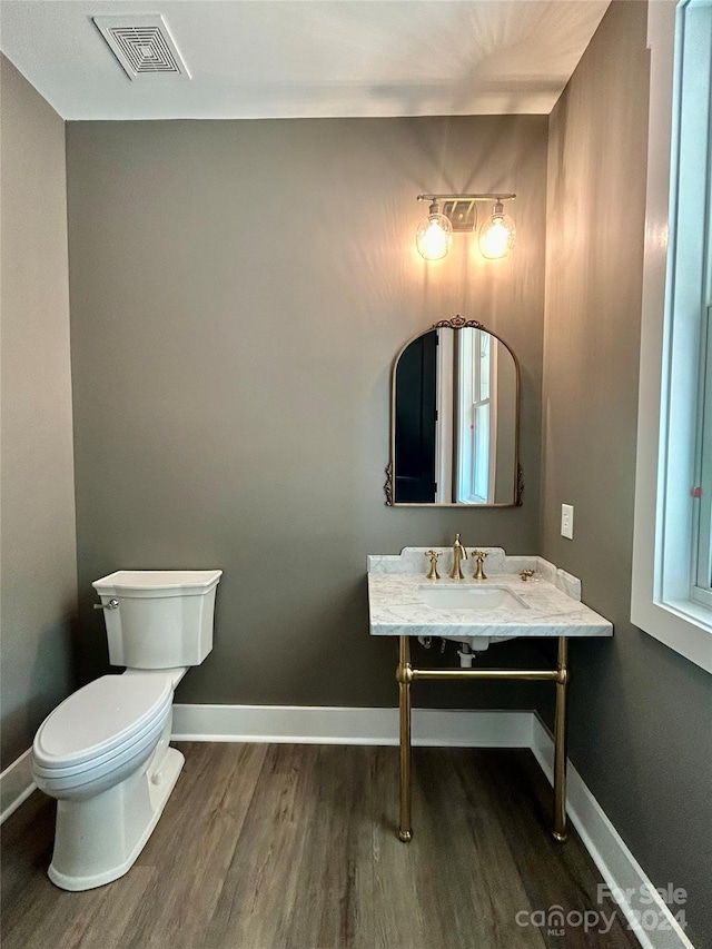 half bath with visible vents, baseboards, and wood finished floors