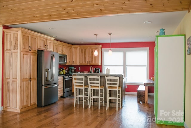 kitchen featuring light brown cabinets, a kitchen breakfast bar, appliances with stainless steel finishes, a center island, and dark wood finished floors