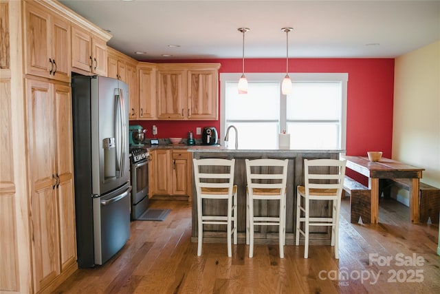 kitchen featuring light brown cabinets, stainless steel appliances, wood finished floors, a kitchen breakfast bar, and a center island with sink