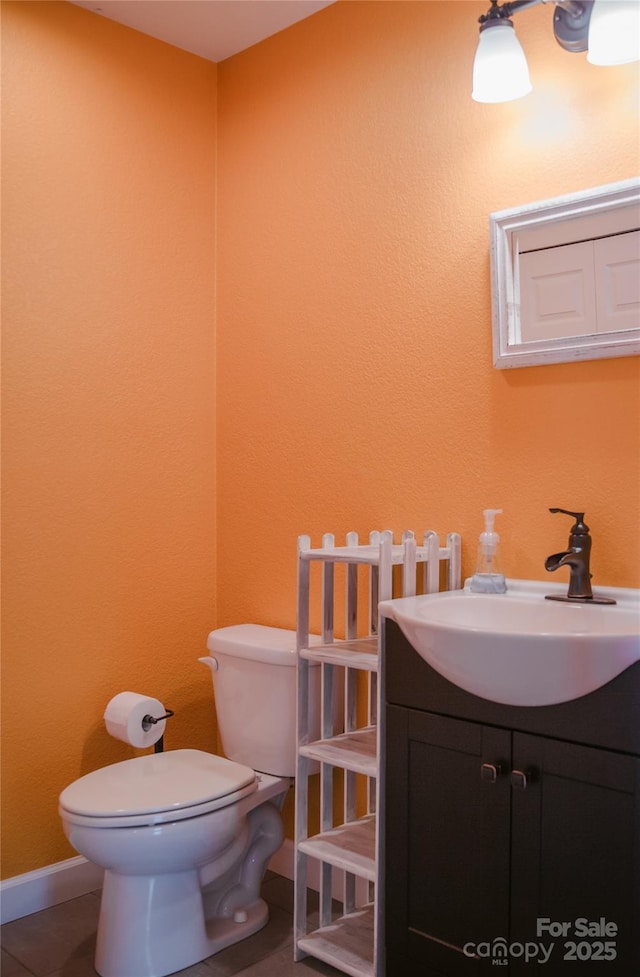 half bathroom featuring tile patterned flooring, baseboards, vanity, and toilet