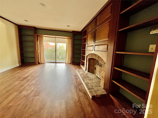 unfurnished living room featuring crown molding, a fireplace, wood-type flooring, and built in shelves