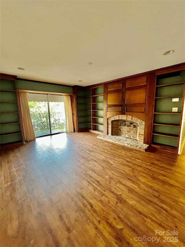 unfurnished living room featuring wood-type flooring, built in shelves, and a fireplace