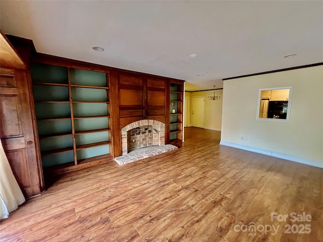 unfurnished living room with a fireplace, an inviting chandelier, light wood-type flooring, built in features, and ornamental molding