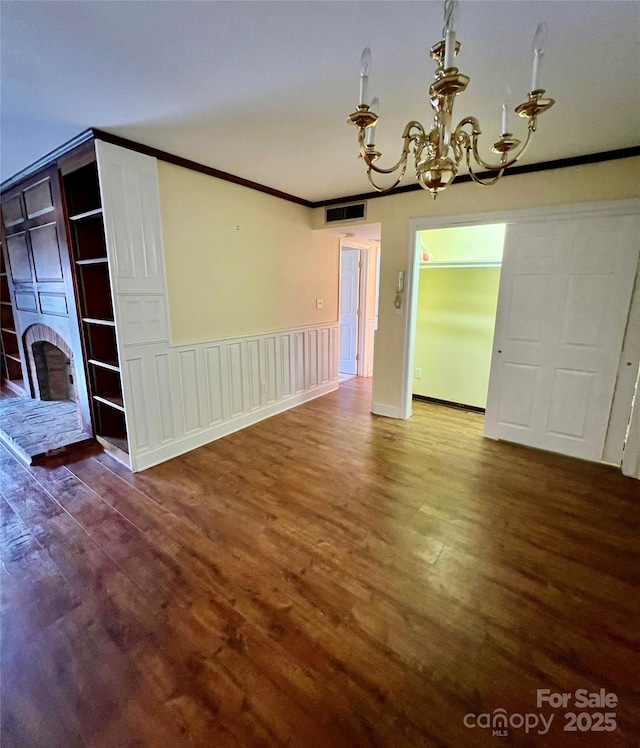 unfurnished dining area with a brick fireplace, crown molding, wood-type flooring, and a notable chandelier