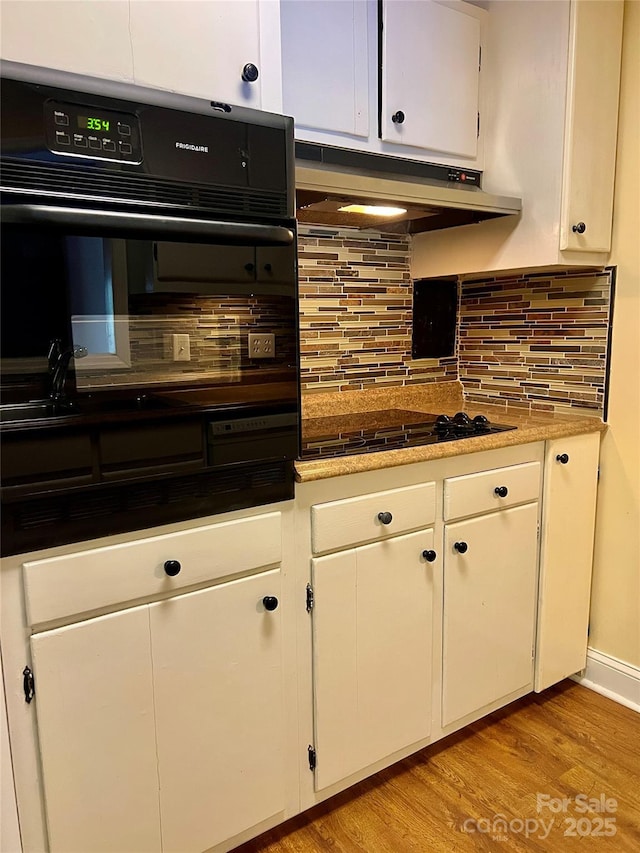 kitchen featuring backsplash, oven, black stovetop, light wood-type flooring, and white cabinets