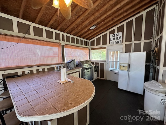 kitchen with tile counters, ceiling fan, white fridge with ice dispenser, and lofted ceiling