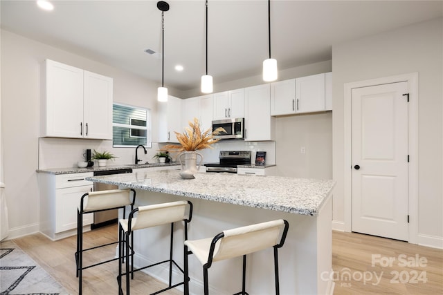 kitchen featuring a kitchen island, white cabinetry, stainless steel appliances, light stone counters, and light hardwood / wood-style flooring